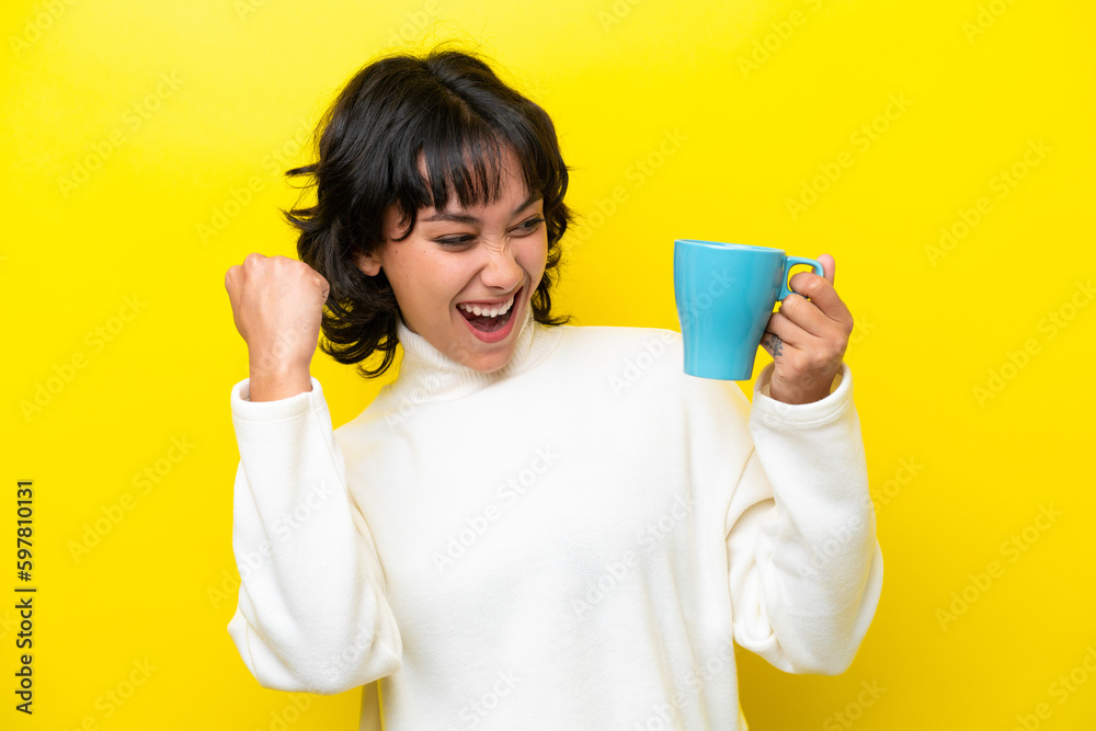 Young Argentinian woman holding cup of coffee isolated on yellow background celebrating a victory Young Argentinian woman holding cup of coffee isolated on yellow background celebrating a victory