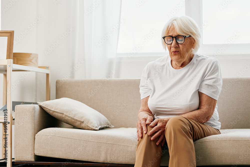 Elderly woman severe pain in her leg sitting on the couch, health