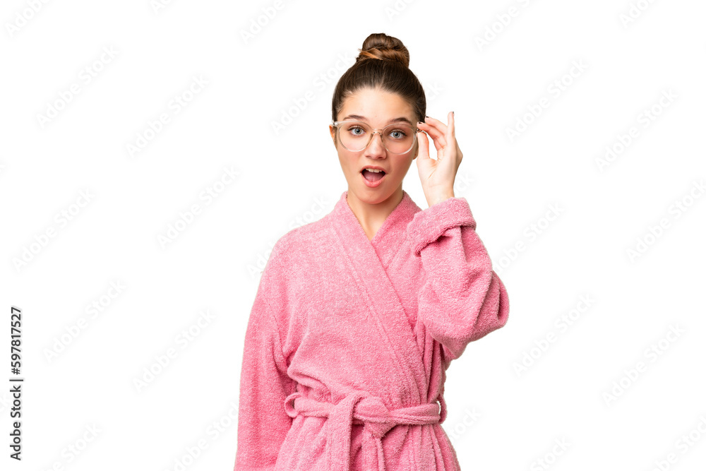 Teenager girl in a bathrobe over isolated chroma key background with glasses and surprised