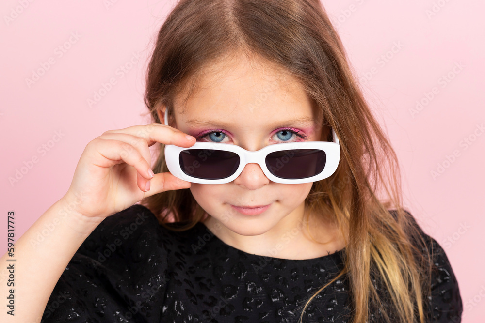Portrait of a Charming little girl in black stylish summer dress, cool white sunglasses and slight pink makeup. Isolated on pink background. Portrait of a Charming little girl in black stylish summer dress, cool white sunglasses and slight pink makeup. Isolated on pink background.