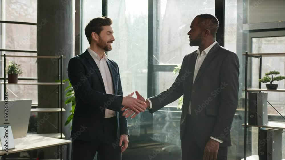 Two diverse businessmen multiracial business partners office coworkers men talking discuss negotiate project handshaking happy shake hands smiling at camera Caucasian man and African worker handshake