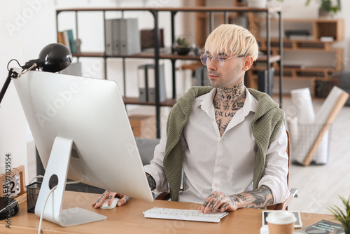 Young tattooed man working with computer at table in office © Pixel-Shot