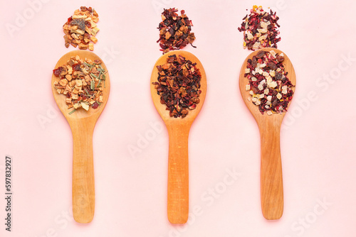 Wooden spoons with different dried fruit tea on pink background