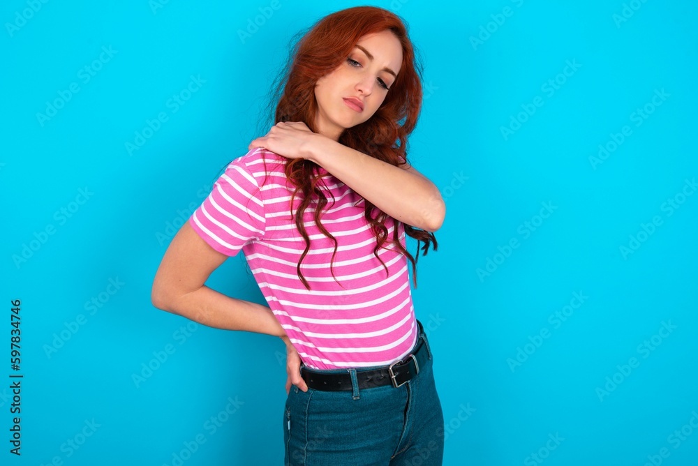 young redhead woman wearing striped T-shirt over blue background got back pain young redhead woman wearing striped T-shirt over blue background got back pain