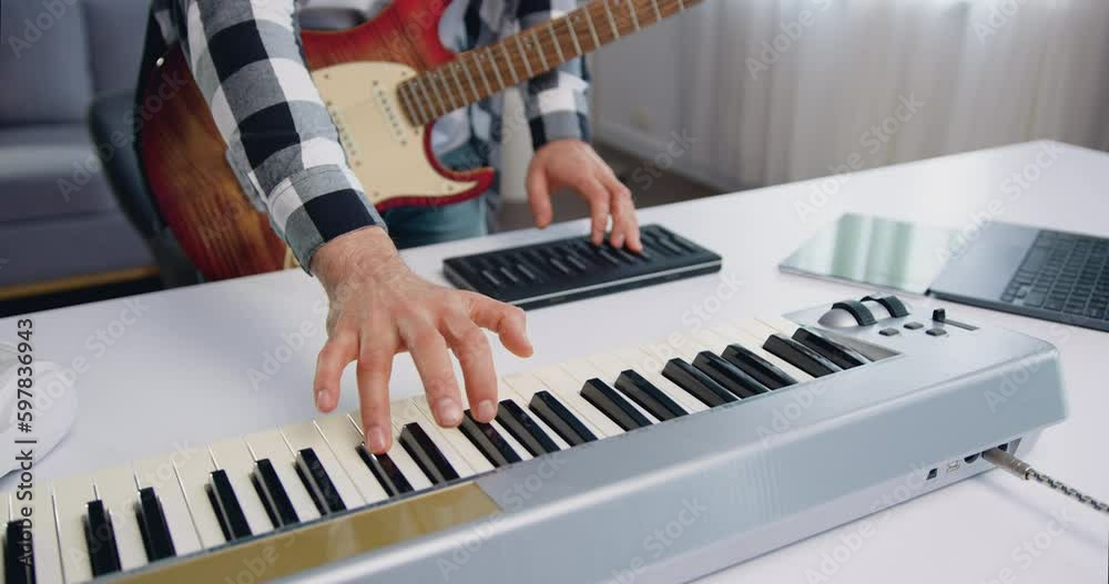 Male hands playing midi piano keyboard in home studio. Man makes electronic music at home. Musician records his composition in a home music studio using professional instruments.