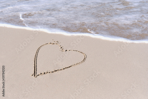 Wave running to heart shape drawn on white sand of tropical beach.