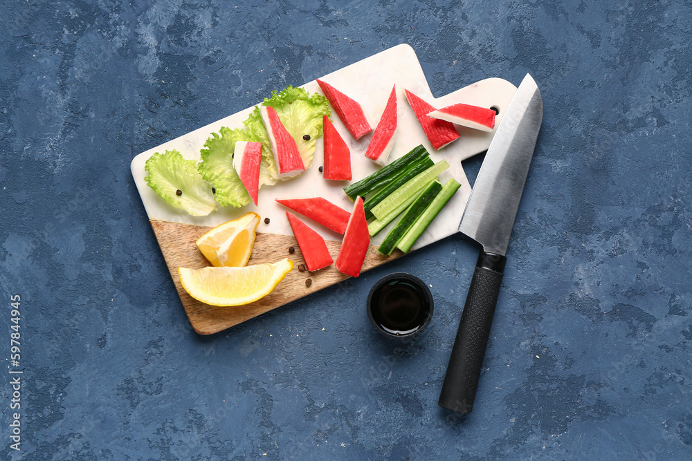 Board with tasty crab sticks and sauce on blue background