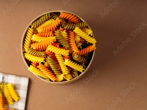 Three colors fusilli pasta on a linen napkin. Green, orange and yellow fusilli pasta stored in eco box. Copy space
