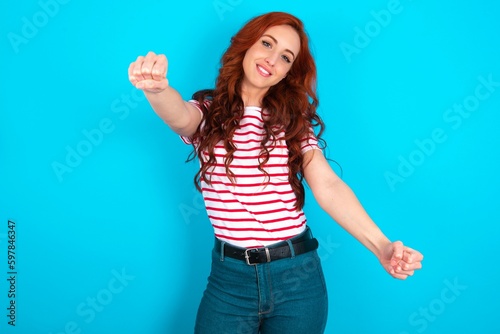 young redhead woman wearing striped T-shirt over blue background imagine steering wheel helm rudder passing driving exam good mood fast speed