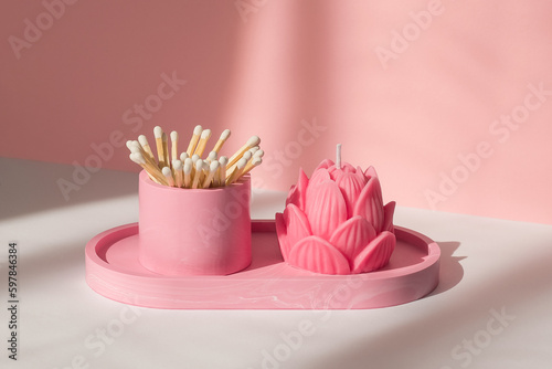 A lotus candle and a glass with matches on a white-pink background.