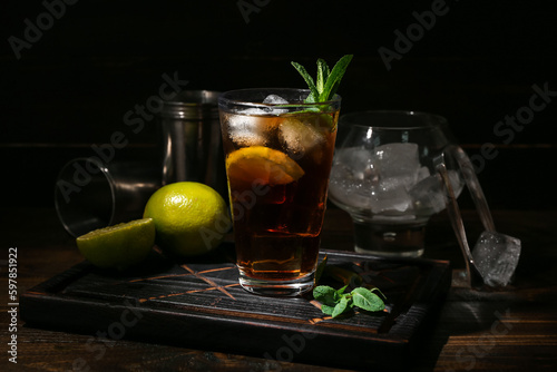 Glass of tasty Cuba Libre cocktail on dark wooden background