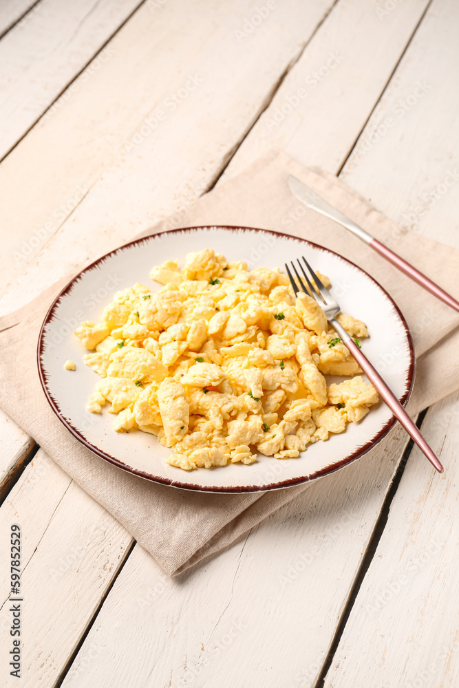 Plate of tasty scrambled eggs with cutlery on white wooden background Plate of tasty scrambled eggs with cutlery on white wooden background