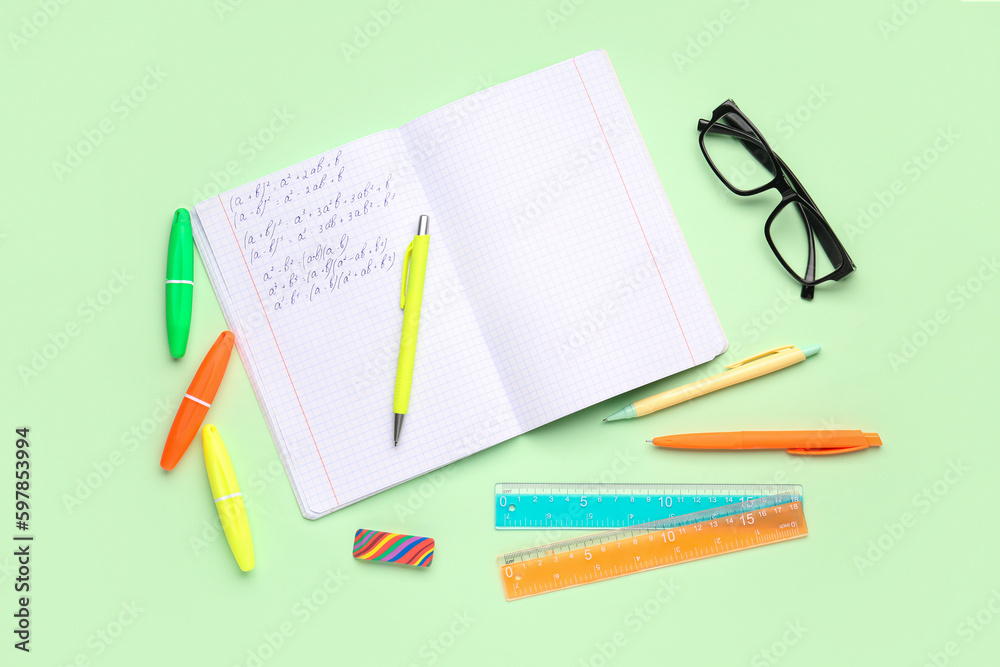 Copybook with maths formulas, glasses and stationery on green background Copybook with maths formulas, glasses and stationery on green background