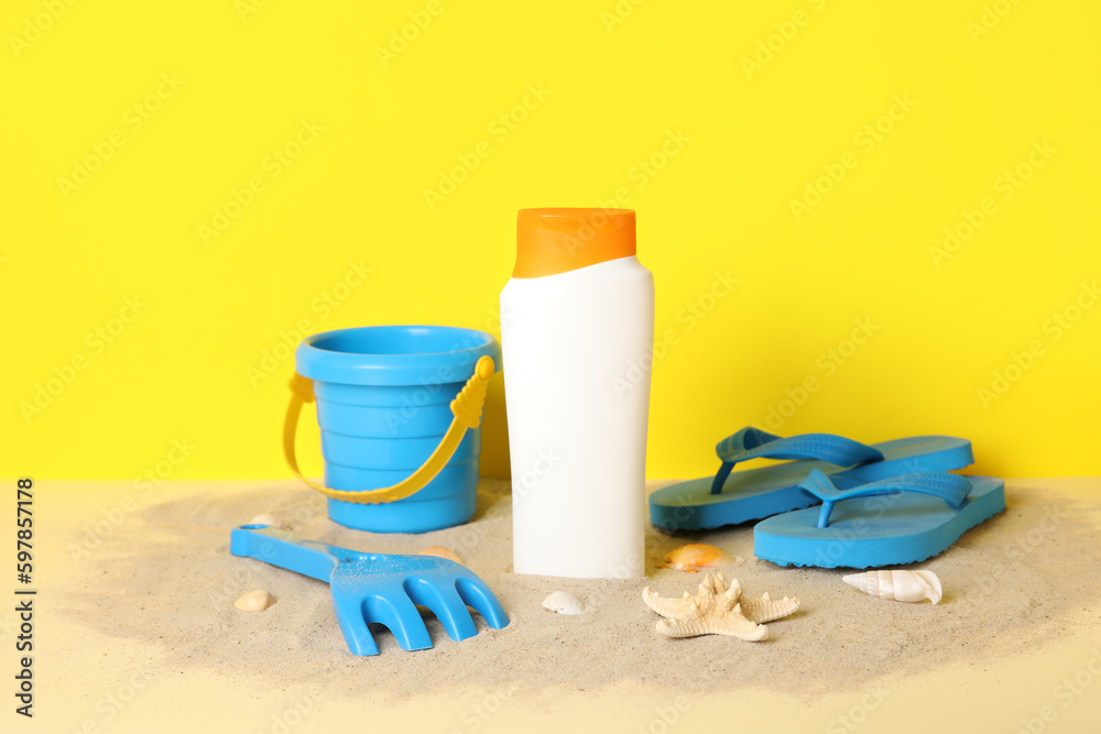 Sunscreen cream for baby with beach accessories on sand near yellow wall Sunscreen cream for baby with beach accessories on sand near yellow wall