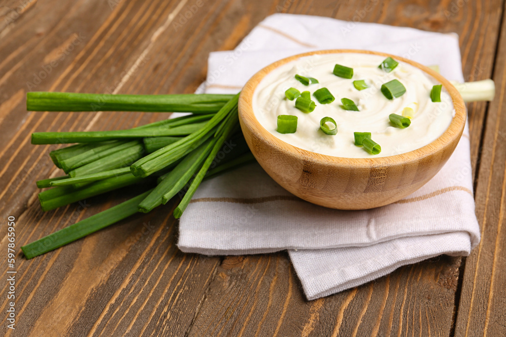 Bowl of tasty sour cream with green onion on wooden background Bowl of tasty sour cream with green onion on wooden background