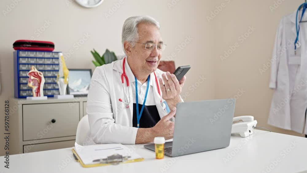 Middle age man with grey hair doctor sending voice message with smartphone at clinic