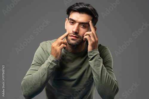 Portrait of young handsome Caucasian man touching and checking wrinkles on his face for skin care and beauty concepts, studio shot isolated on light gray background