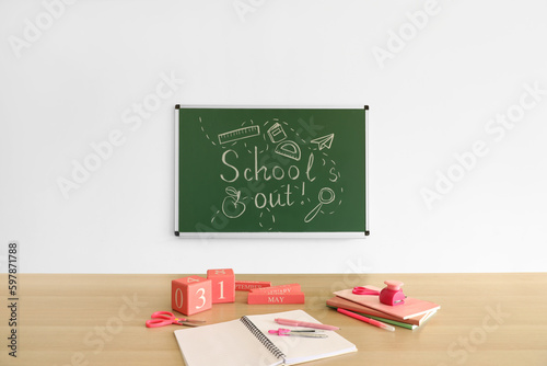 Blackboard with text SCHOOL'S OUT, drawings and desk in classroom