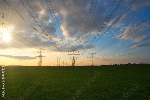 A lot of high-voltage power line, electrical energy transmission tower overhead line masts, high voltage pylons as power pylons on the fields