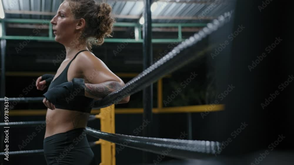 Female athlete rests on the ring ropes after a boxing fight. Attractive female muay thai fighter takes break between rounds in training in gym Female athlete rests on the ring ropes after a boxing fight. Attractive female muay thai fighter takes break between rounds in training in gym