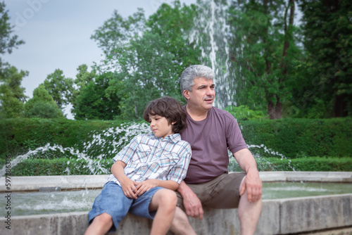 Dad and son are relaxing in the city park near fountains. Family have fun. Happy fathers day.