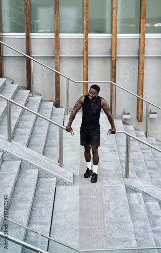 Fit happy sporty young black man standing at urban stairs feeling confident. Strong African ethnic guy doing sport fitness street workout exercises or jogging, resting after training outside. Vertical © insta_photos
