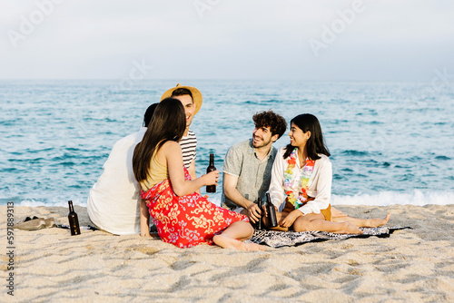 Happy young friends social gathering sitting on the beach in summer vacation. Friendship lifestyle and vacation concept