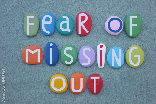 Fear of missing out, creative message composed with multi colored stone letters over green sand