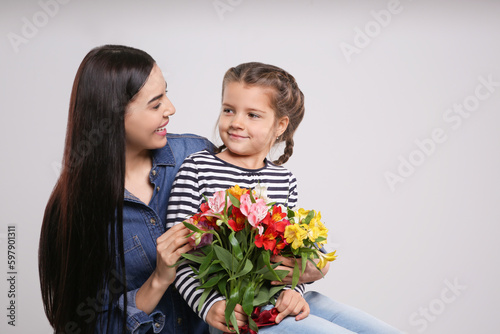 Happy woman with her cute daughter and bouquet of beautiful flowers on light grey background, space for text. Mother's day celebration