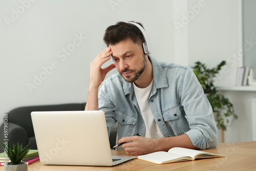 Man in headphones studying on laptop at home. Online translation course © New Africa