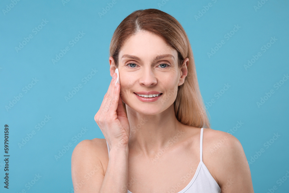 Beautiful woman removing makeup with cotton pad on light blue background Beautiful woman removing makeup with cotton pad on light blue background