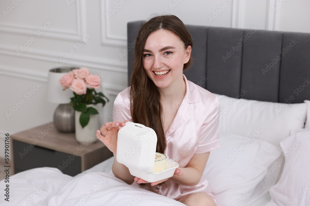 Beautiful young woman holding her Birthday cake on bed in room Beautiful young woman holding her Birthday cake on bed in room