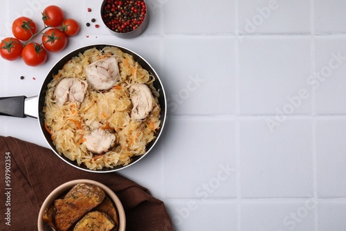 Frying pan with sauerkraut, chicken and products on white tiled table, flat lay. Space for text