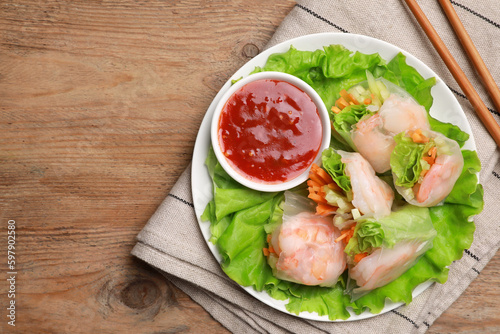 Tasty spring rolls served with lettuce and sauce on wooden table, top view. Space for text
