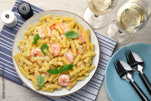 Delicious pasta with shrimps, basil and parmesan cheese served on light wooden table, flat lay