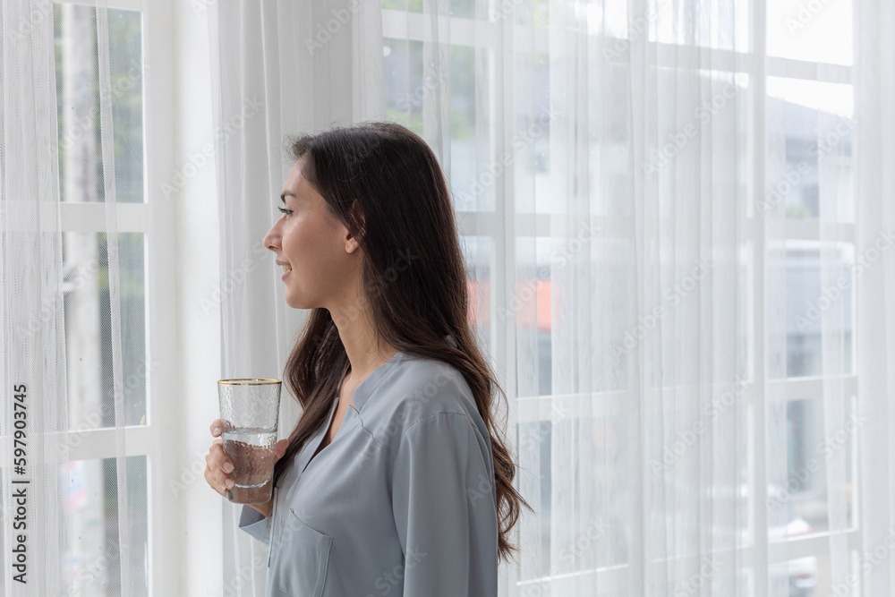 Smiling Young Woman Drinking Water by the Window at Home Smiling Young Woman Drinking Water by the Window at Home