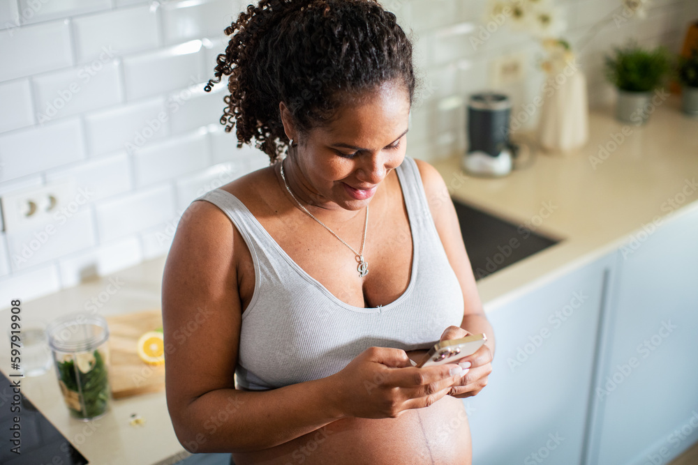 Young pregnant latina woman using a smart phone in the kitchen of a home Young pregnant latina woman using a smart phone in the kitchen of a home