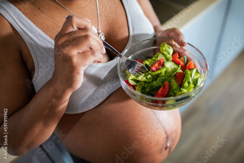 Young pregnant latina woman eating a salad in the kitchen of a home