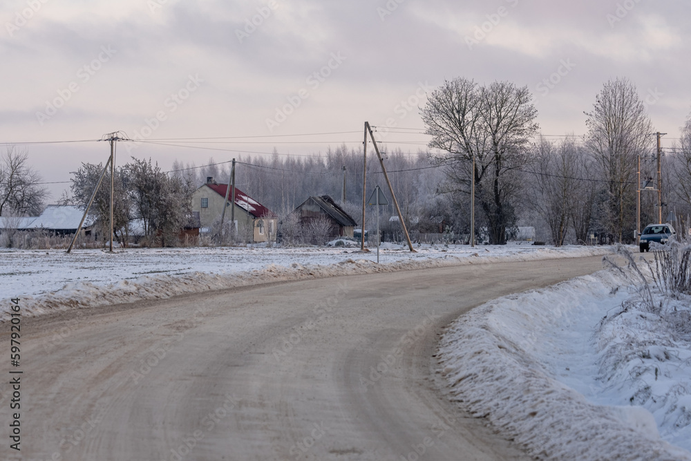 winter rural scene with snow covered trees, houses, electricity poles and country road. Latvia
