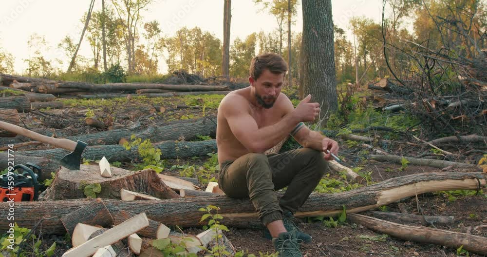 Shirtless tired sweaty man with muscular body smoking cigarettes having rest in the forest, taking break after hard work slow motion tiredness. Smoking break