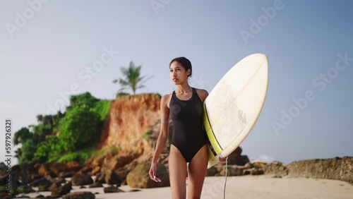African american woman walking with surfboard on ocean beach. Black female surfer going with surf board. Pretty multiethnic girl goes on surfing session at sunrise. Slow motion, slomo.