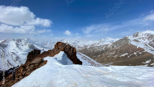 Amazing aerial view of snow covered mountain peaks. Mountain landscape. Blue sky and white clouds. Red rocks. Natural calm background.