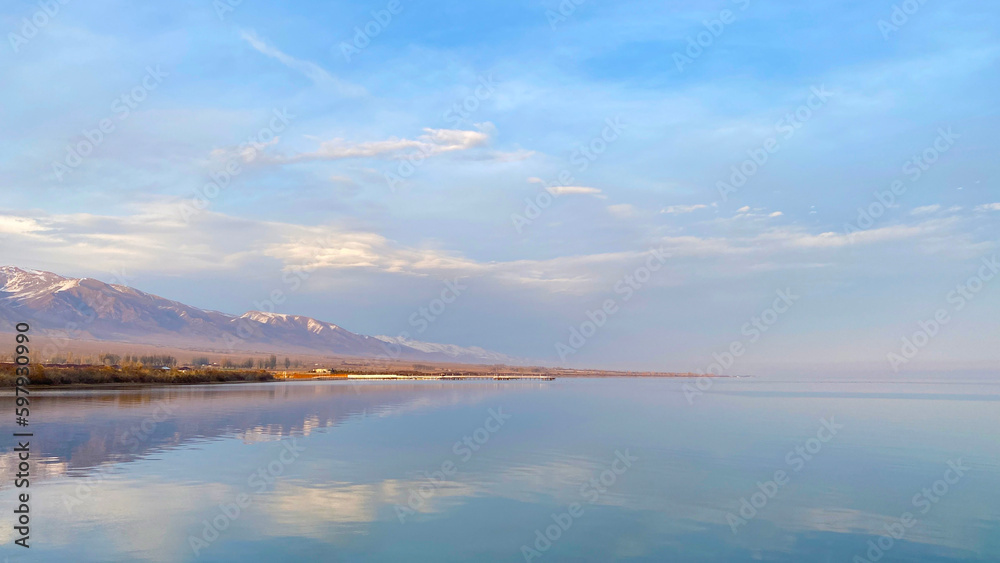 Amazing view of the clear mountain clear lake Issyk-Kul, Kyrgyzstan. The calm surface of the water. Beautiful seascape. Blue sky with white clouds.