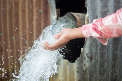 Water is coming out of a pipe and a boy is catching the water