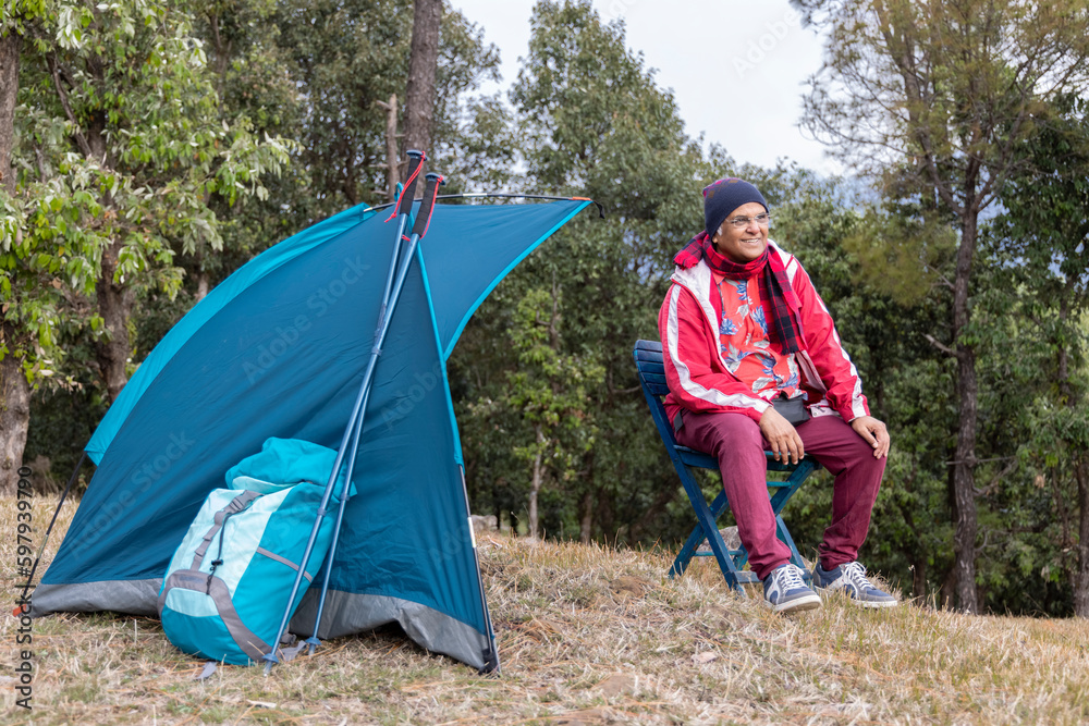Fototapeta premium Active Senior Man Camping in Mountains. Sitting in a front of his Tent on Camping Chair.