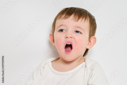 Bored baby yawns with open mouth, studio white background. Screaming child with an emotion of displeasure on his face. Kid about two years old (one year nine months)