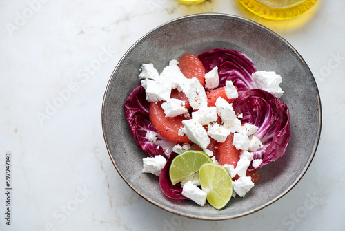 Grey plate with radicchio, goat cheese and grapefruit salad, horizontal shot on a light-beige marble background
