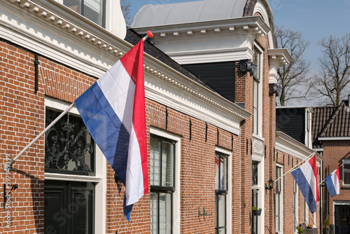 Dutch flags waving in a typical dutch street on Koningsdag under a blue sky. Koningsdag is a national holiday in the Kingdom of the Netherlands. 