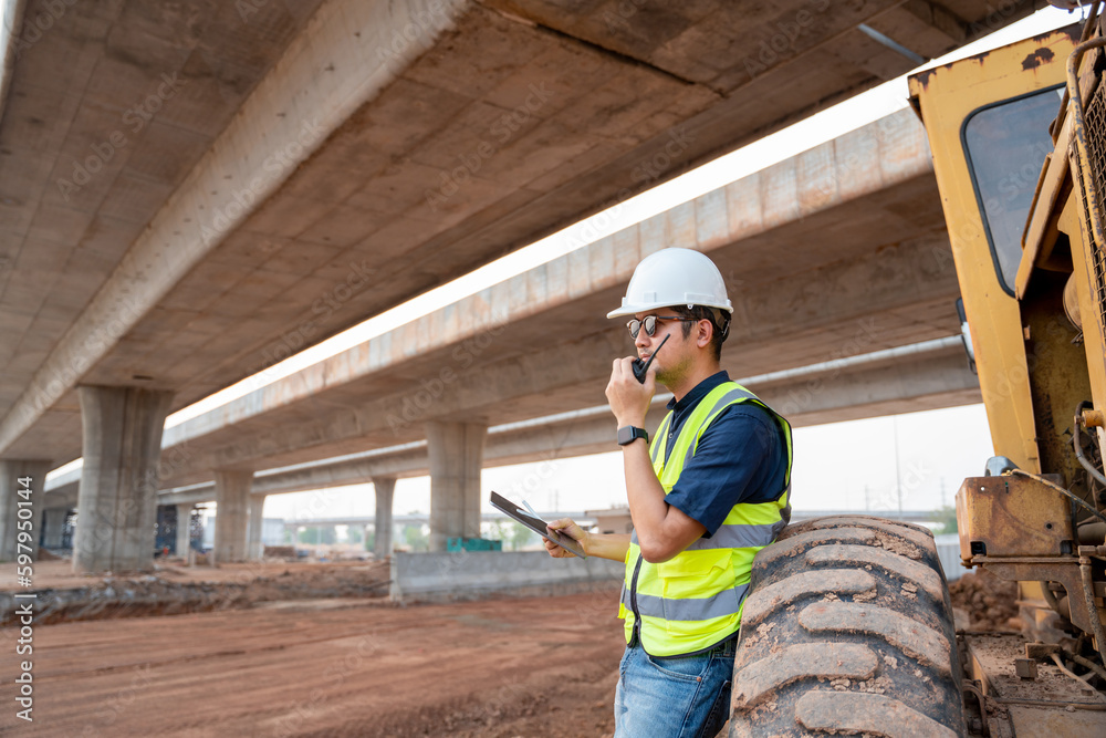 A civil engineer working beside the wheels of grader industrial machine at a road construction site. A civil engineer working beside the wheels of grader industrial machine at a road construction site.