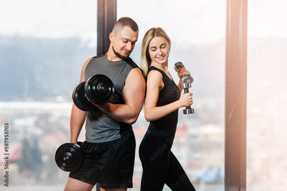 Sporty young couple working out with dumbbells by the window at home. Sporty young couple working out with dumbbells by the window at home.